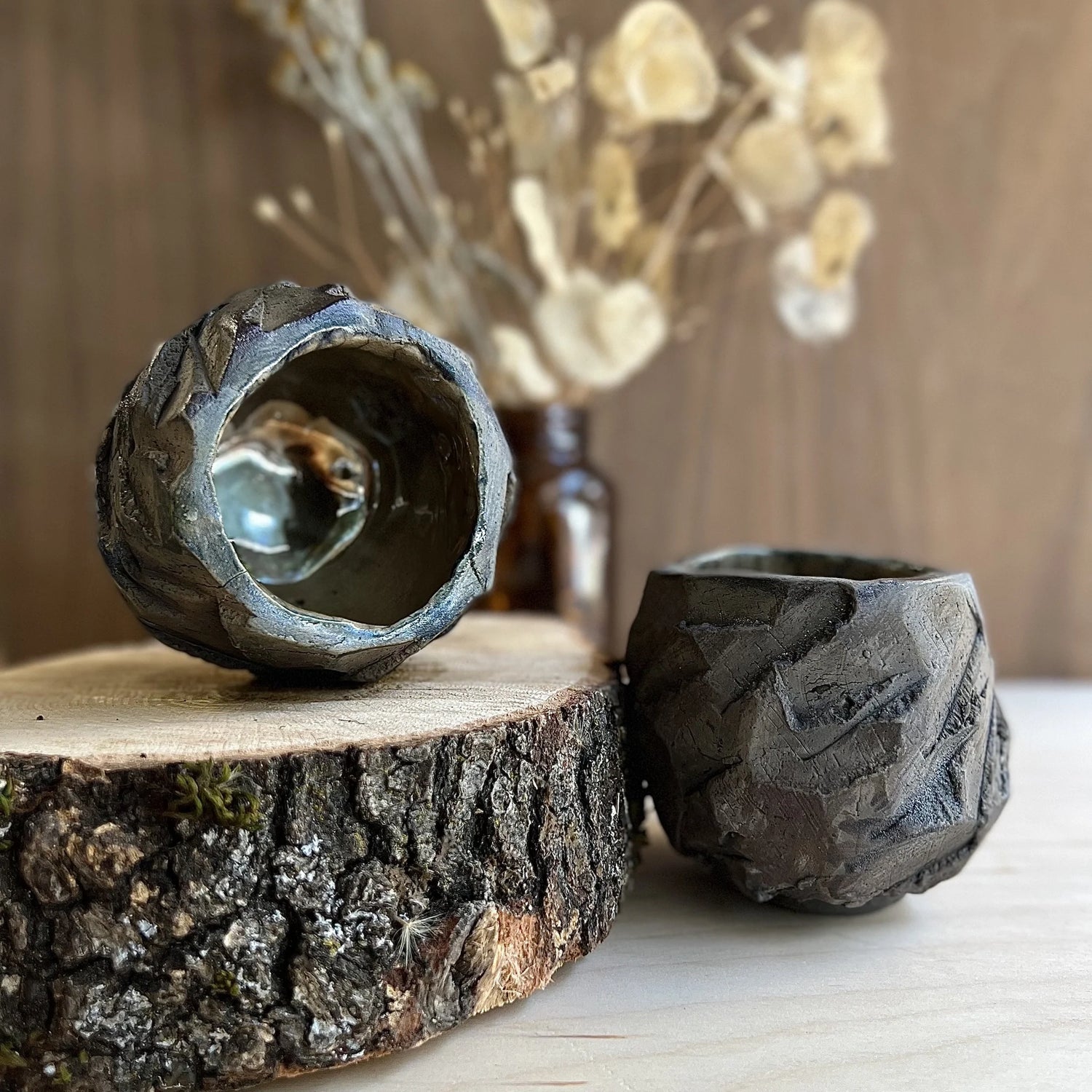 Image of two hand carved grey ceramic kurinuki cups with dried flowers and wood