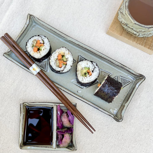Black ceramic sushi tray with sushi, set of chopsticks, soy sauce tray with salad and sake cup