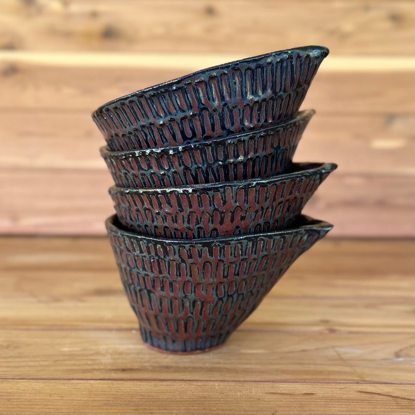 stack of four little carved ceramic espresso cups against a wood background with a black and red bronze glaze