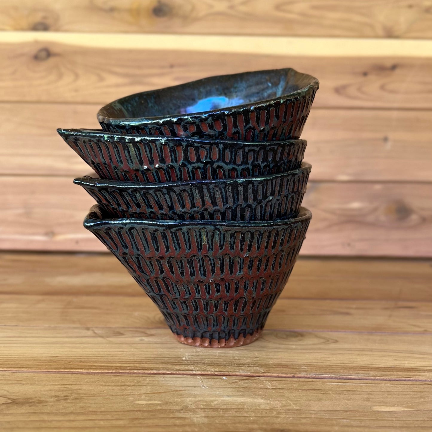 stack of four little carved ceramic espresso cups against a wood background with a black and red bronze glaze