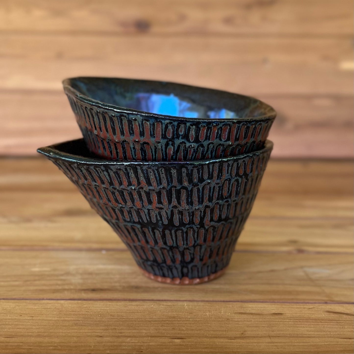 stack of two little carved ceramic espresso cups against a wood background with a black and red bronze glaze