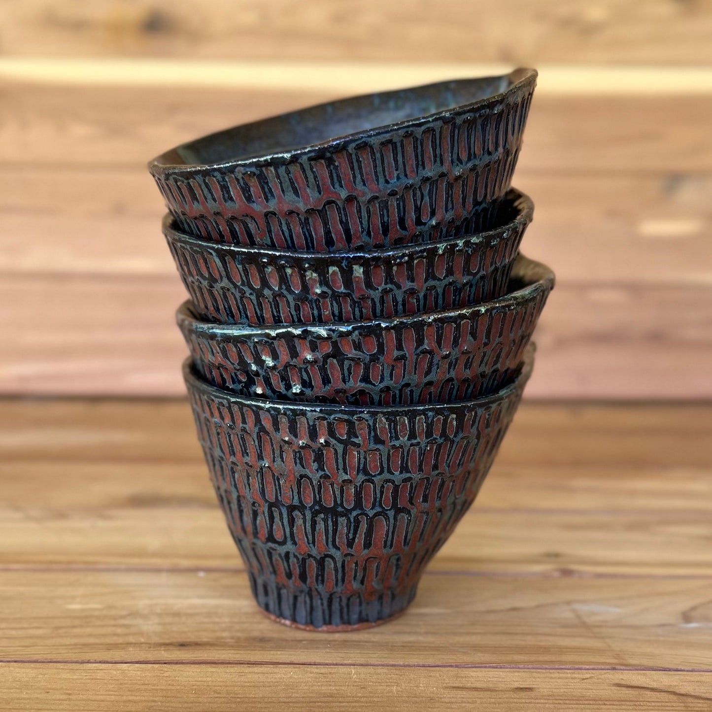 stack of four little carved espresso cups with a black and red bronze glaze