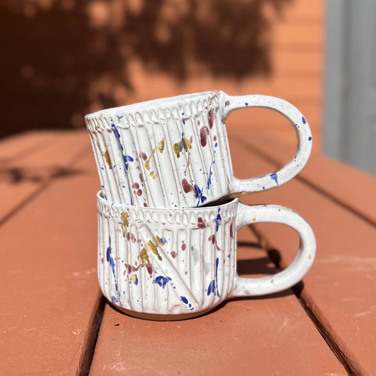 Two large white ceramic paint splatter mugs
