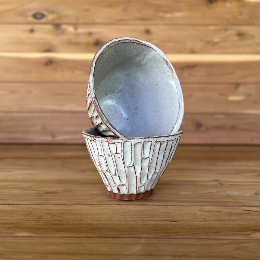 two small hand carved red clay espresso cups against a wood background