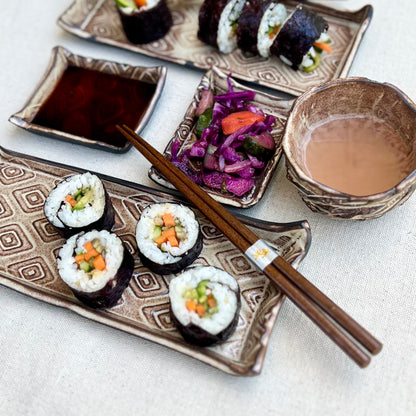 Textured black and gold ceramic sushi set with sushi, soy sauce, and sake cup