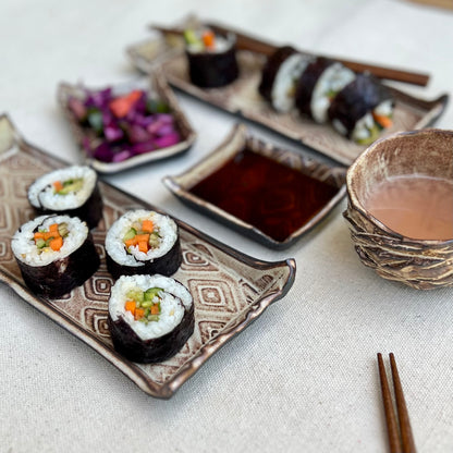 Textured black and gold ceramic sushi set with trays, soy sauce dishes, and sake cup with display sushi