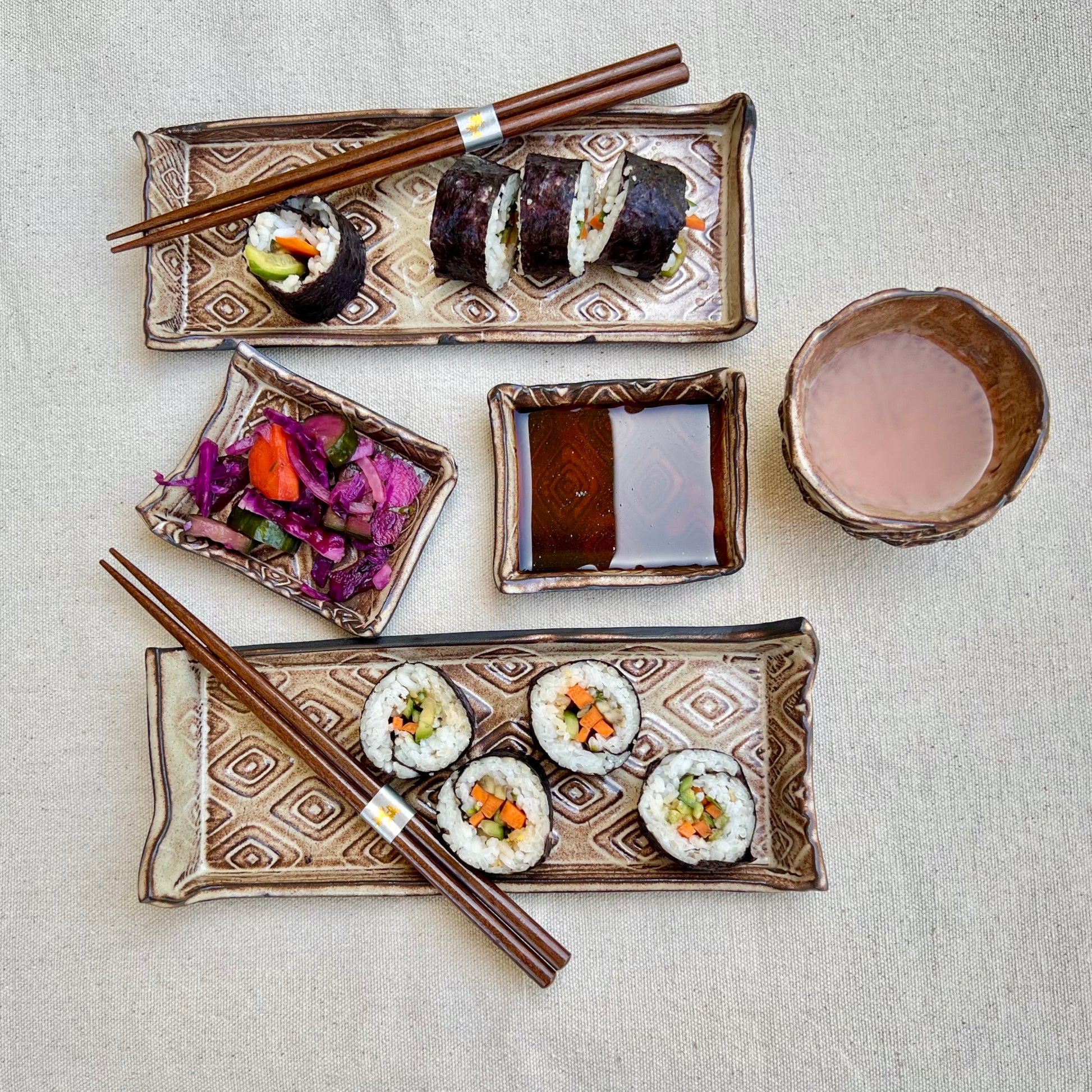 Textured black and gold ceramic sushi set with trays, soy sauce dishes, and sake cup with display sushi