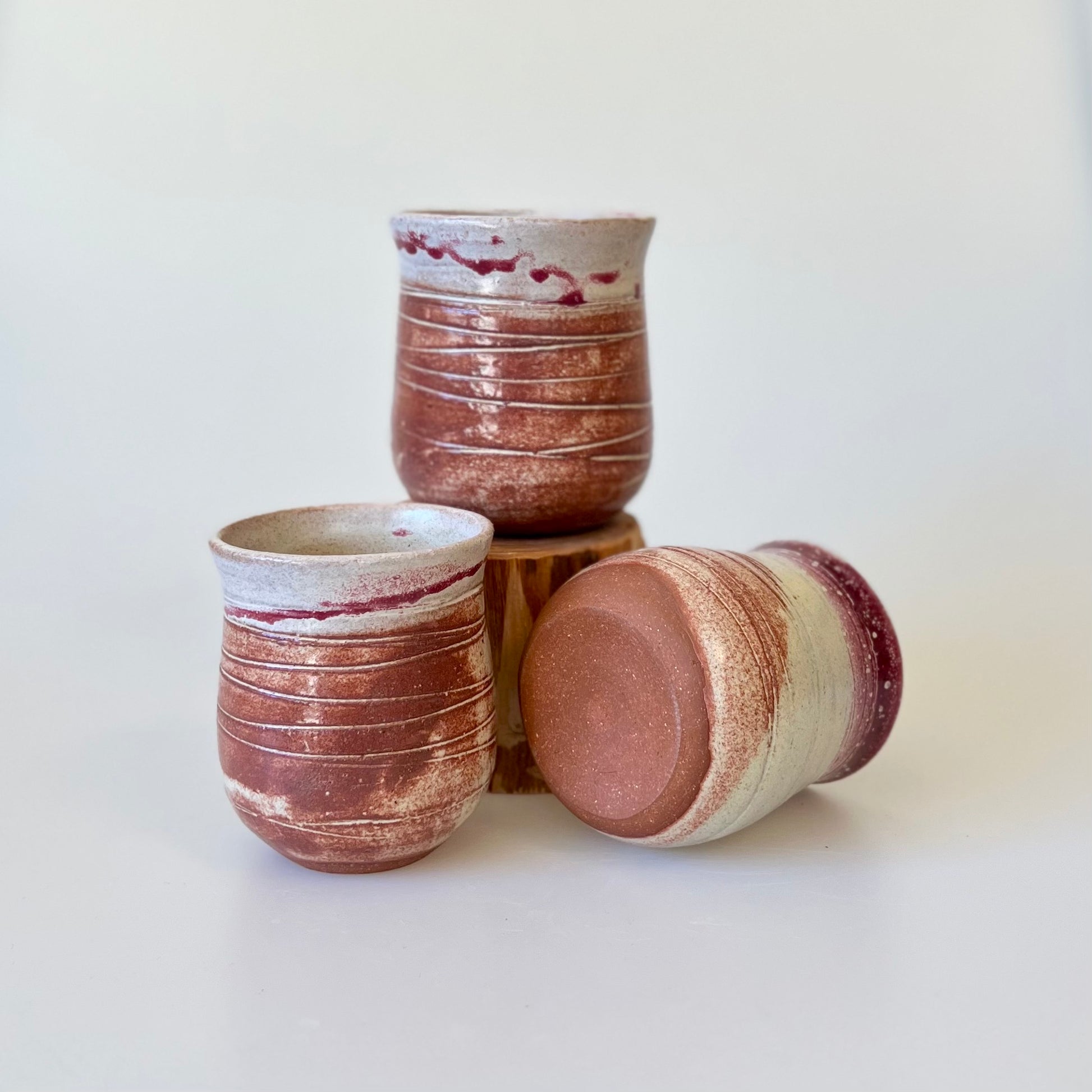 three small stemless red ceramic round wine tumblers