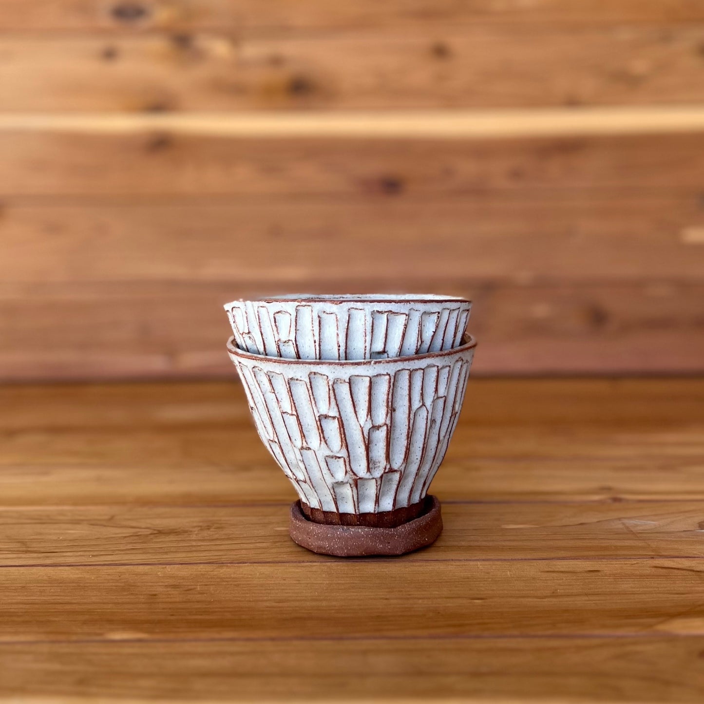 image of two small hand carved red clay espresso cups against a wood background