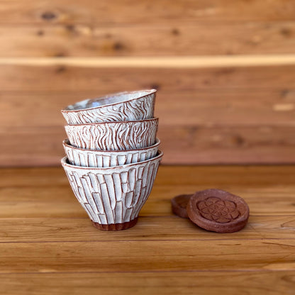 four small hand carved red clay espresso cups with saucers against a wood background