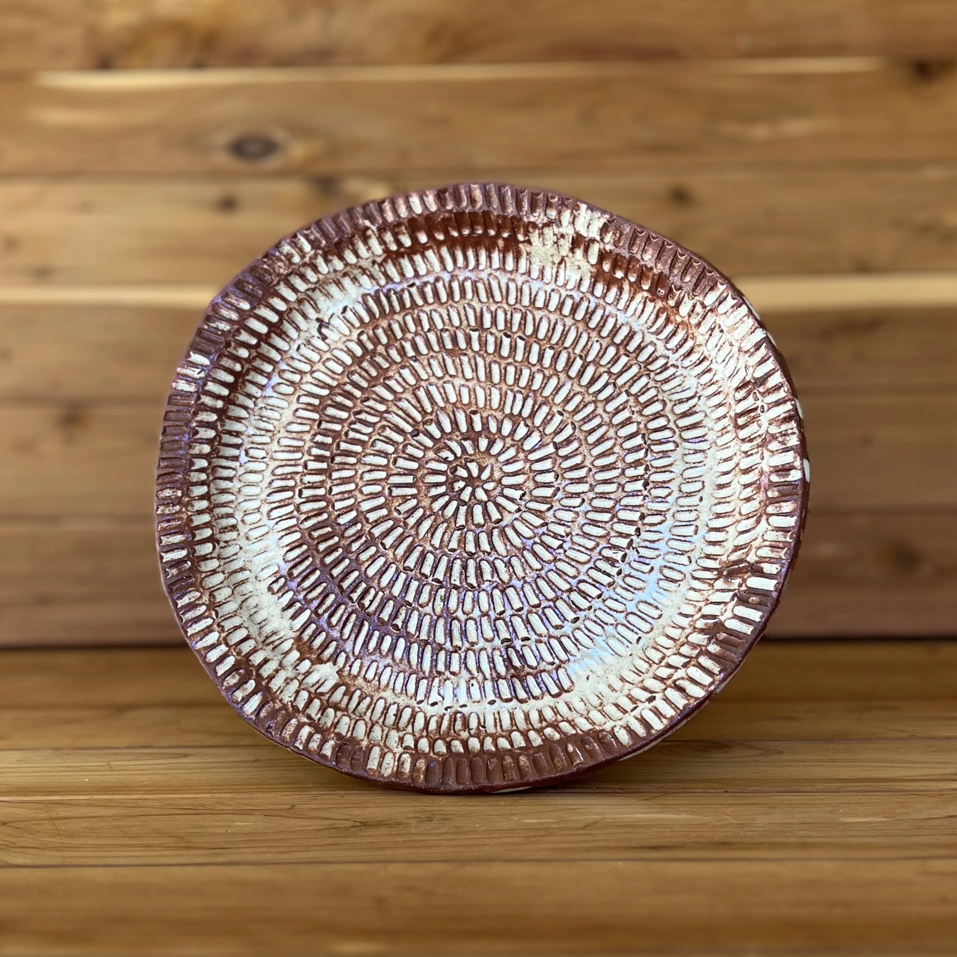 image of one large carved red clay dinner plate in front of wood 