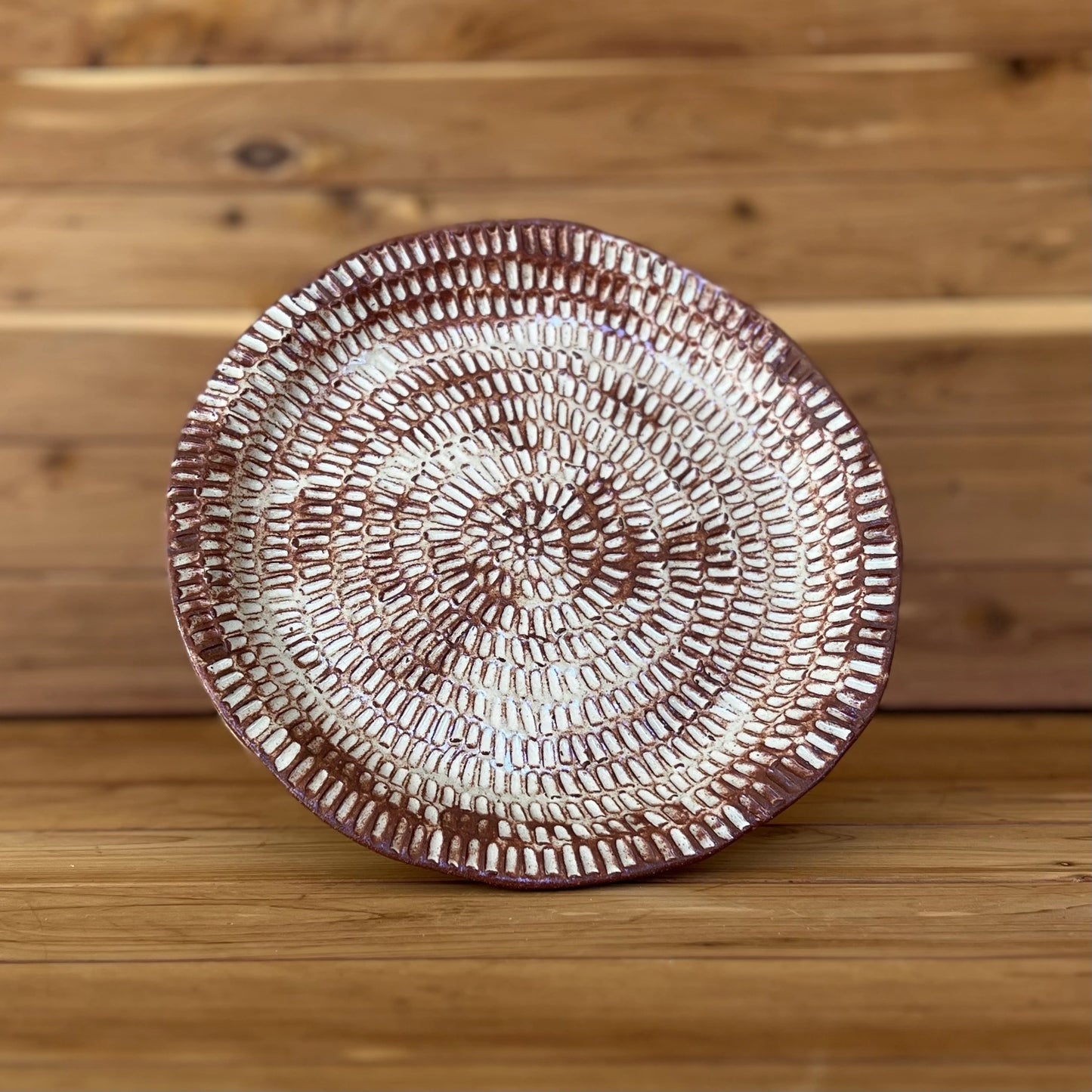 image of one large hand carved red clay plate in front of wood