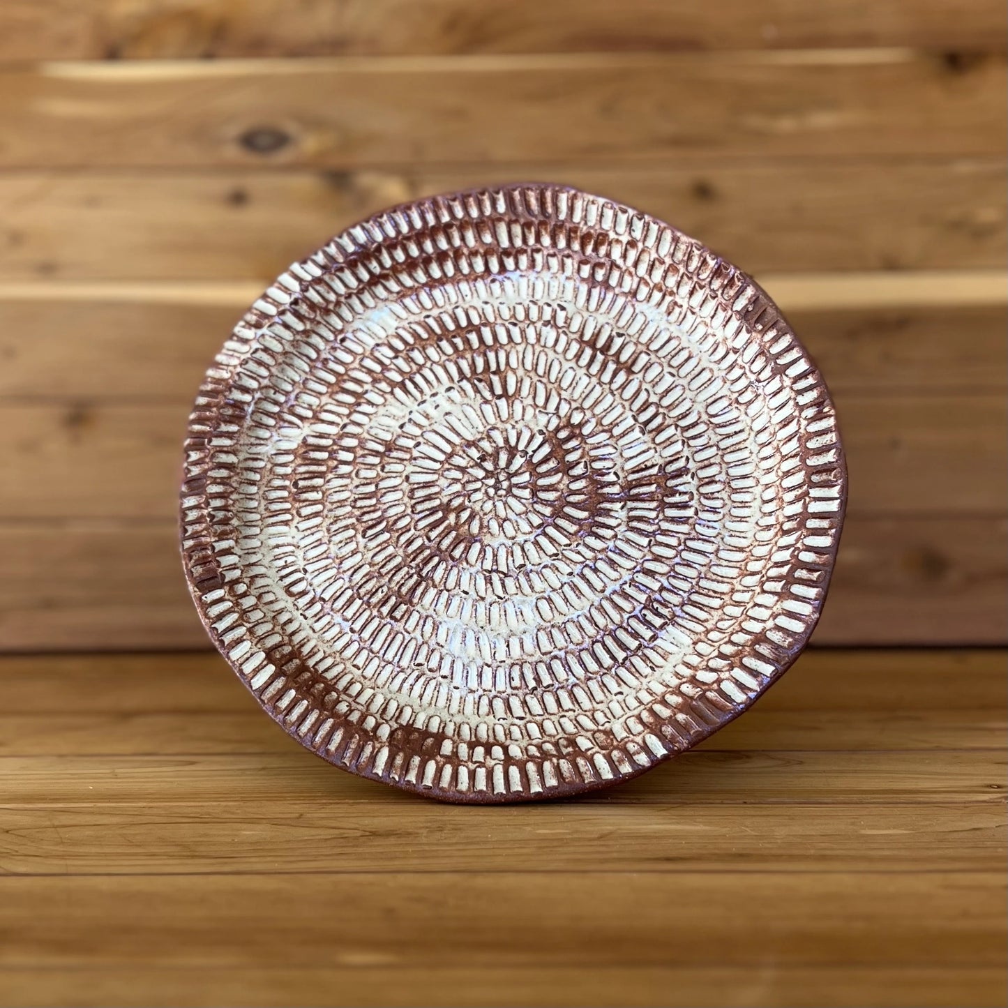 image of one large hand carved red clay plate in front of wood