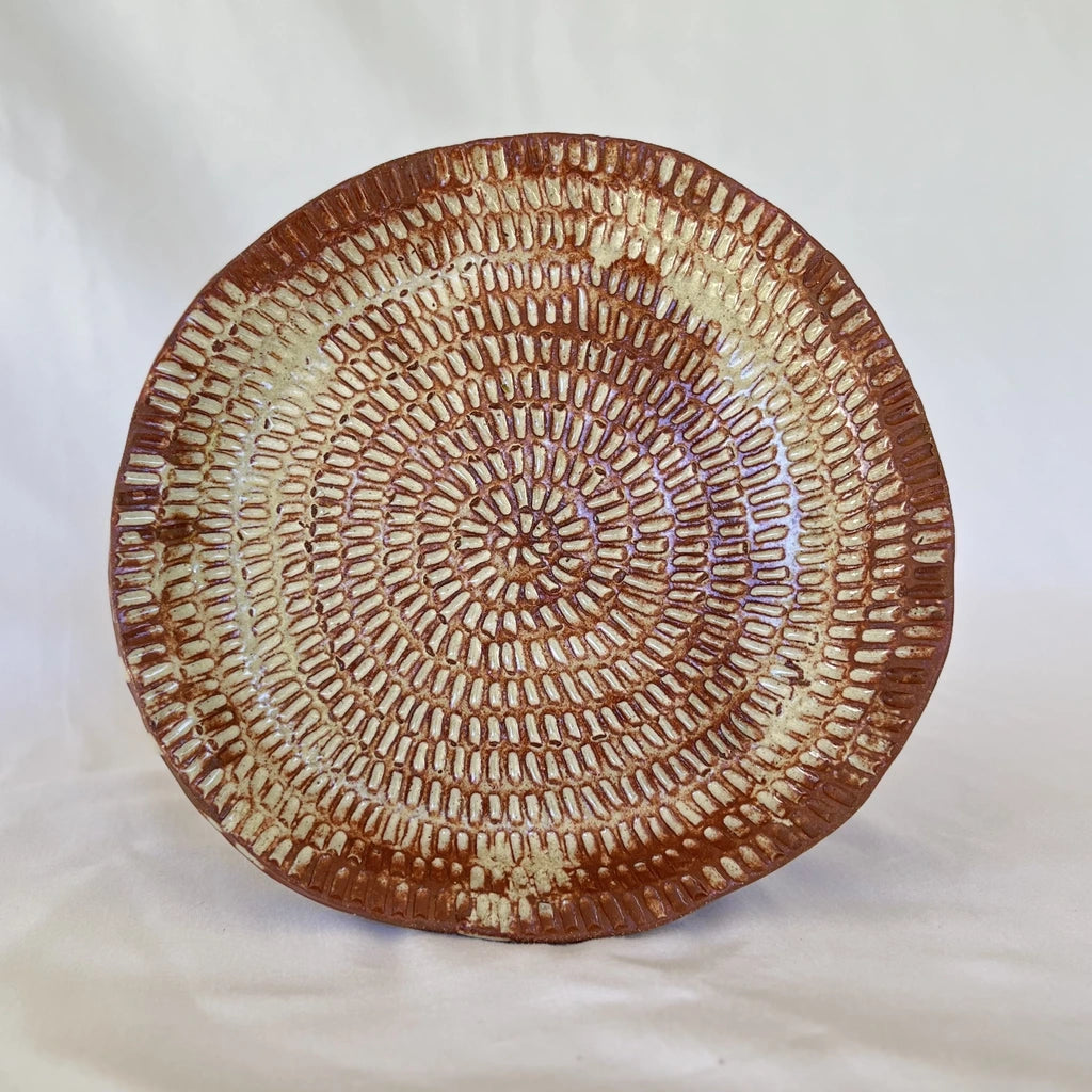 image of one large intricate hand carved red clay plate in front of a white background