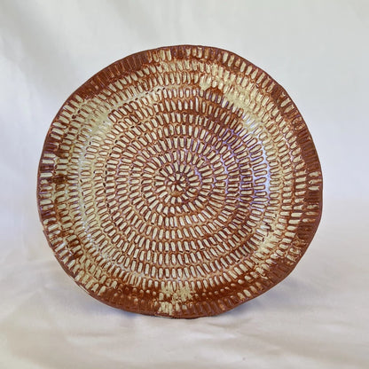 image of one large intricate hand carved red clay plate in front of a white background