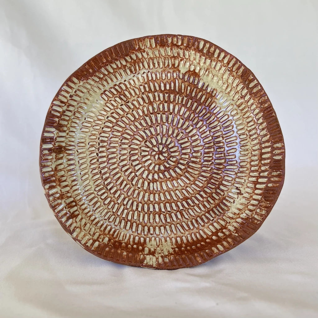 image of one large intricate hand carved red clay plate in front of a white background