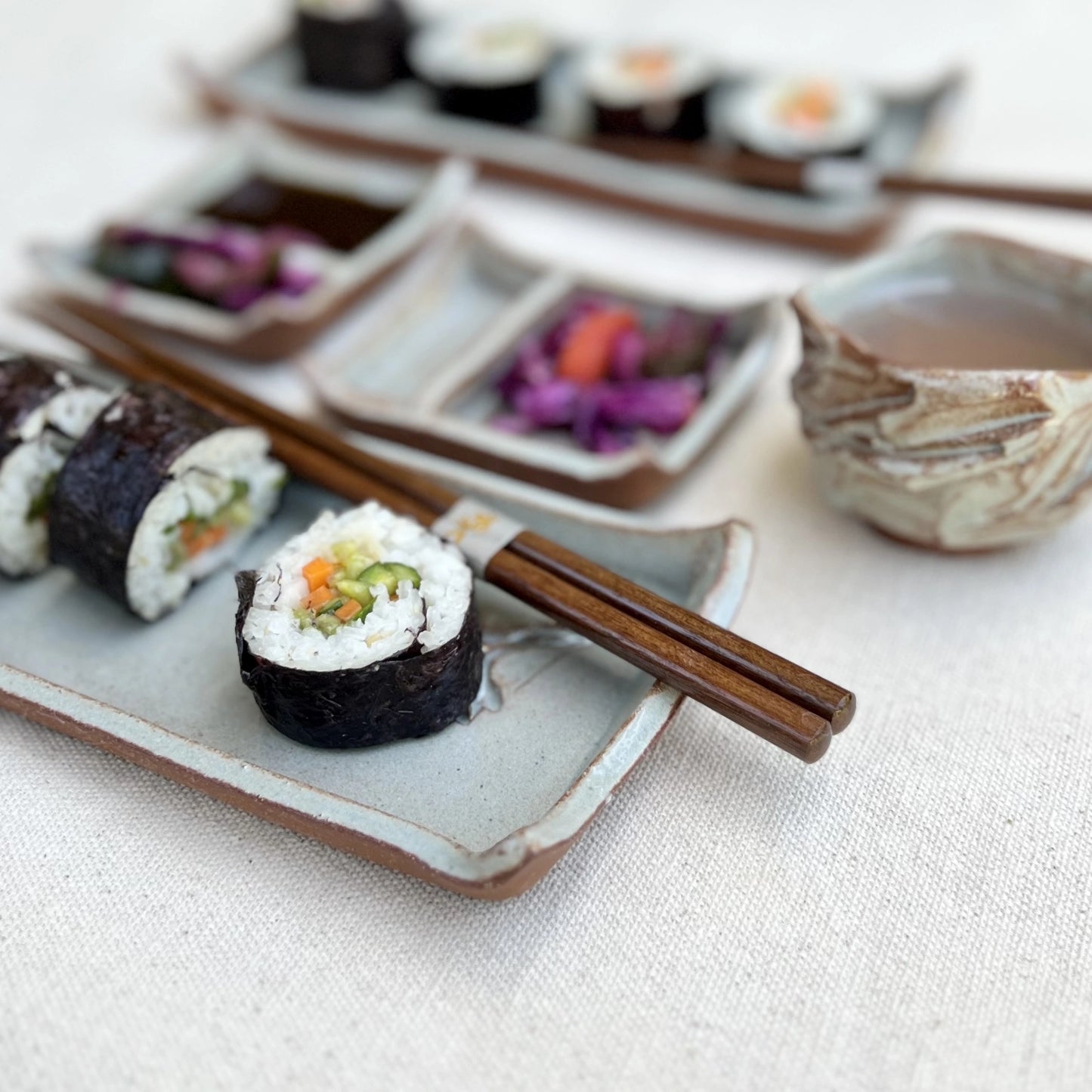 rustic ceramic sushi set with sushi, soy sauce, and kurinuki cup