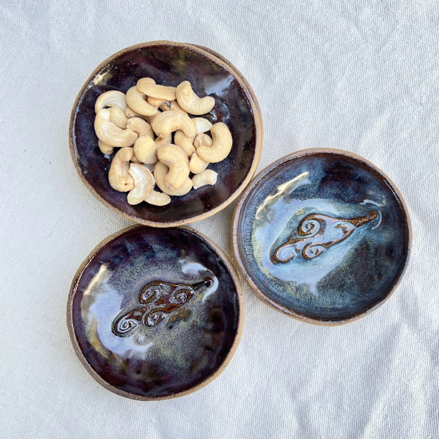 Three small ceramic snack bowls with galaxy glaze and cloud stamp with cashews